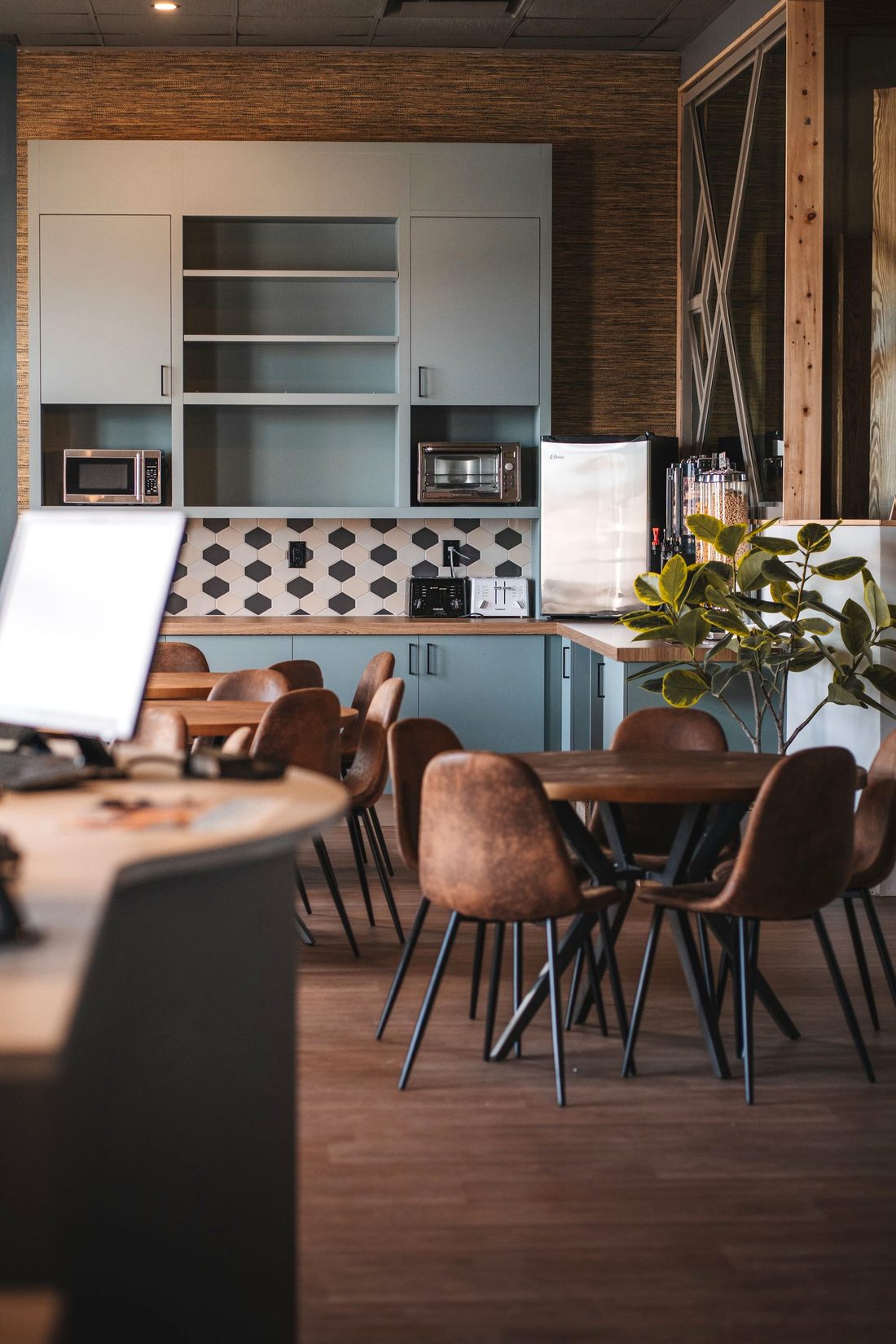 A bright, modern office break room with teal cabinets, a snack-and-coffee station, and casual seating