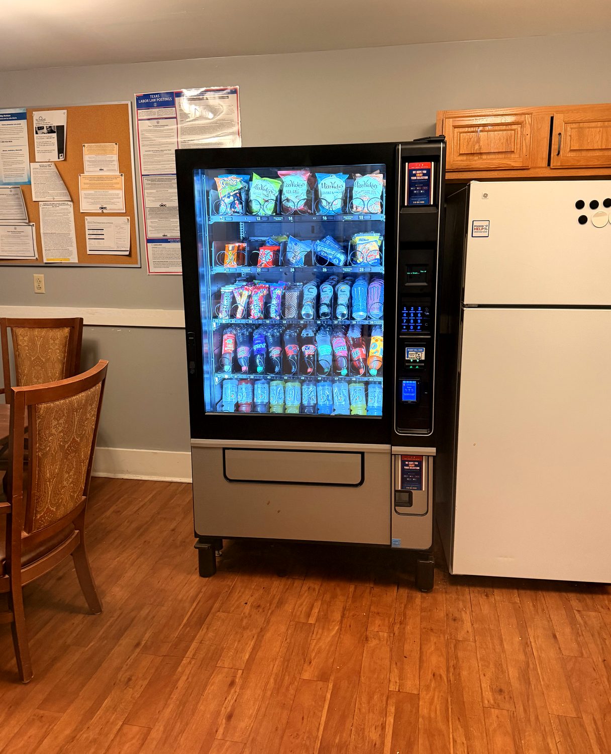 Combo snack and drink vending machine installed in an office break room next to a refrigerator